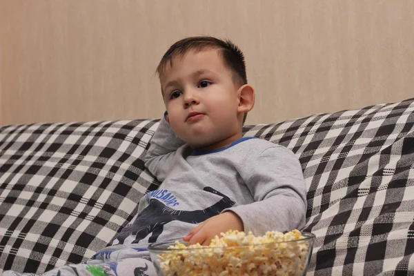 Piccolo ragazzo sul divano a guardare la TV e mangiare popcorn di notte i — Foto Stock