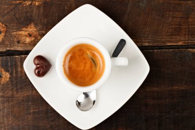 Küçük espresso bardağı ve çikolatalı kalp, cilalanmış masaya karşı.