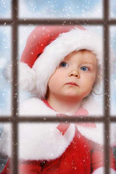 Vue à travers la fenêtre sur bébé fille mignonne dans le chapeau de Père Noël — Photo