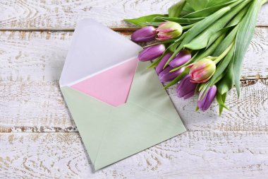 Bir sürü taze lale ve ahşap zemin üzerinde duran zarfın içinde bir mektup. 