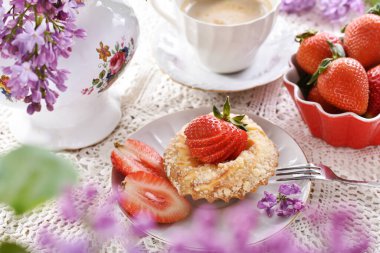 Süzme peynirli ve çilekli ev yapımı mini tart, kırmızı kasede taze meyve ve bir fincan kapuçino.