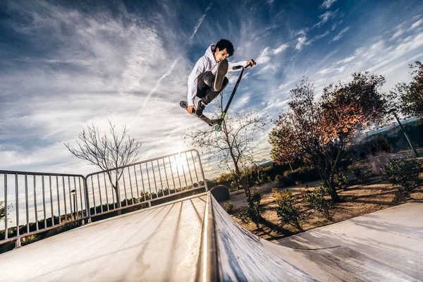 Skatepark bir atlama günbatımı sırasında yapma scooter ile genç adam — Stok fotoğraf