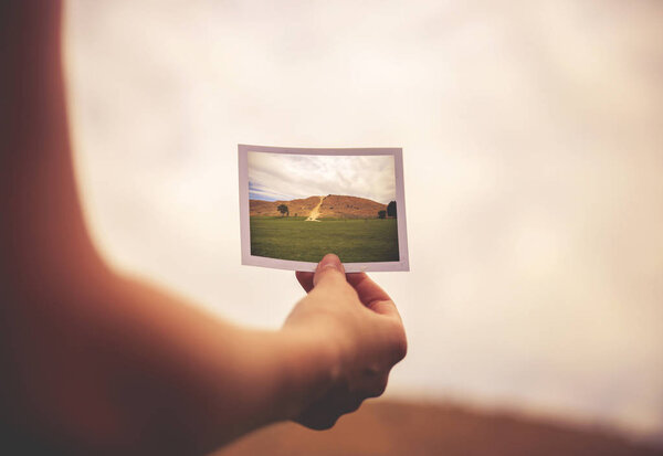a woman holding an instant photo of a hill