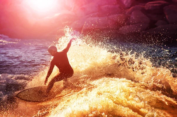 Into the sun photo of a surfer riding a wave in a full wet suit — Stock Photo, Image