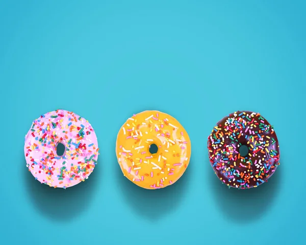 Donuts com cobertura colorida e polvilhas em um estúdio de fundo azul isolado filmado em cima com sombras — Fotografia de Stock