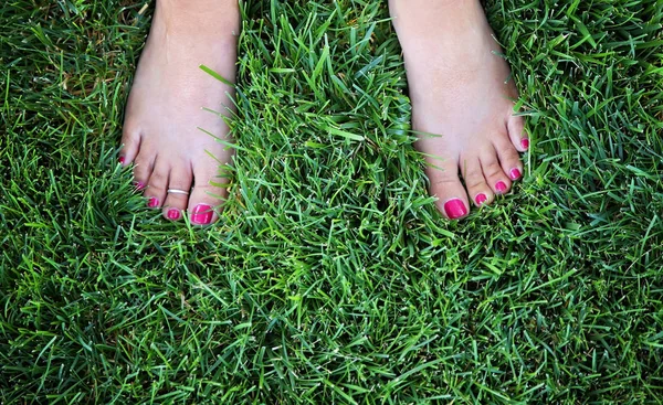 Pés descalços bonita de uma mulher em pé na grama verde exuberante com unhas pintadas e um anel do dedo do pé em — Fotografia de Stock