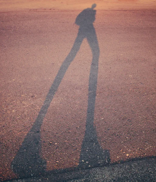 Long shadow of a person walking along a curb in a parking lot during sunrise or sunset toned with a retro vintage instagram filter — Stock Photo, Image