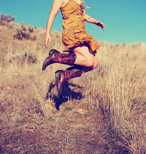 Pretty woman in a skirt jumping up in cowboy boots in a wheat field on a hot summer day toned with a retro vintage instagram filter — Stock Photo, Image