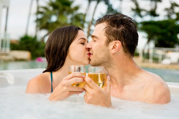 Paar in jacuzzi zoenen met wijnglazen in handen — Stockfoto