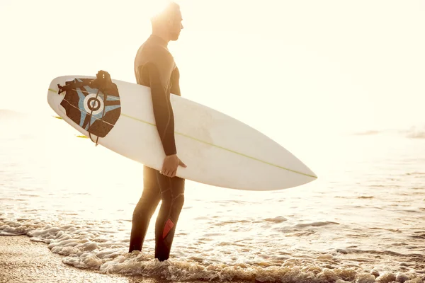 Surfer with surfboard standing at beach — Stock Photo, Image