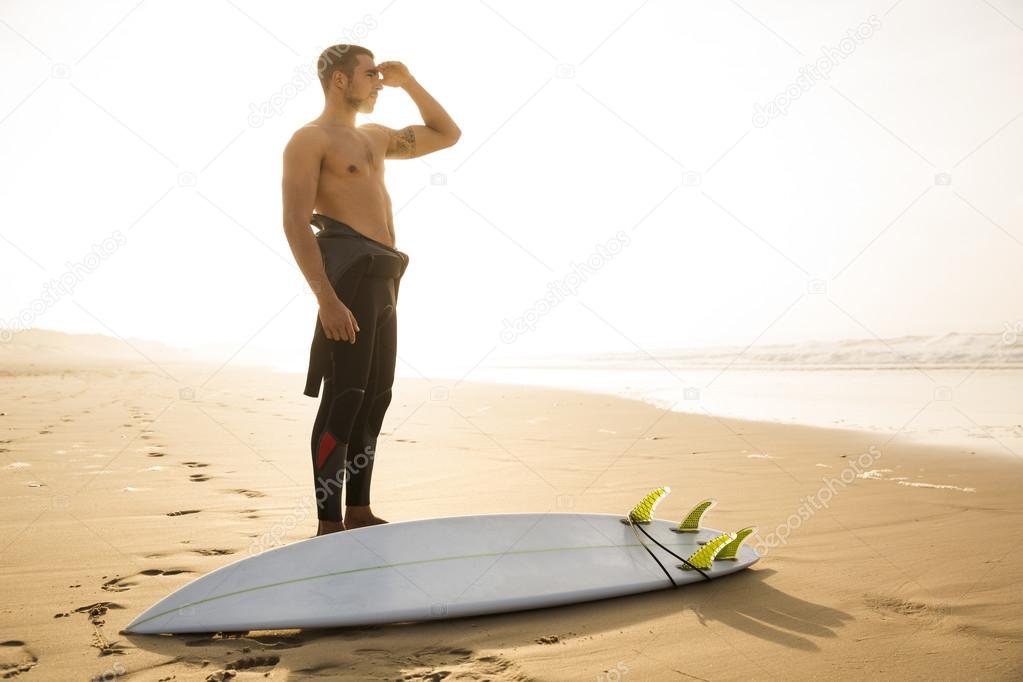 surfer standing at beach looking to waves