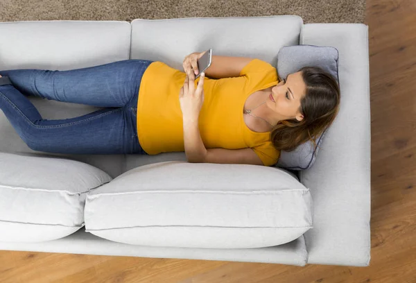 女性はソファに横になっていると電話を使用して — ストック写真