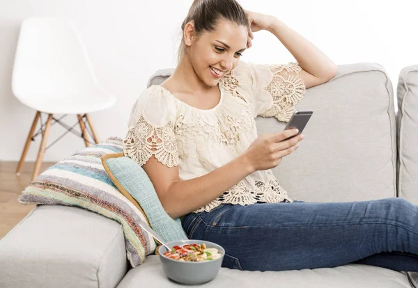 Woman sitting on sofa with phone — Stock Photo, Image