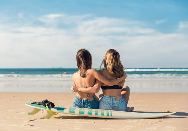 Duas Amigas Bonitas Praia Sentadas Areia Com Pranchas Surf Abraçando — Fotografia de Stock