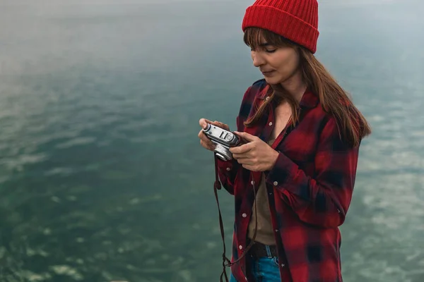 美丽的女人手持相机在湖岸边的多云天 — 图库照片