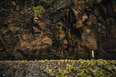Woman walking near rocky wall, Azores, Portugal clipart