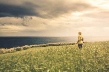 Kadın sarı montlu bulutlu günde okyanus için arıyorsunuz