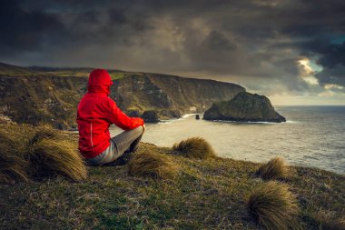 Woman sitting on ground and looking to sea, Azores, Portugal clipart