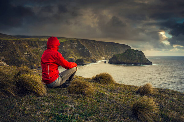 Woman sitting on ground and looking to sea, Azores, Portugal