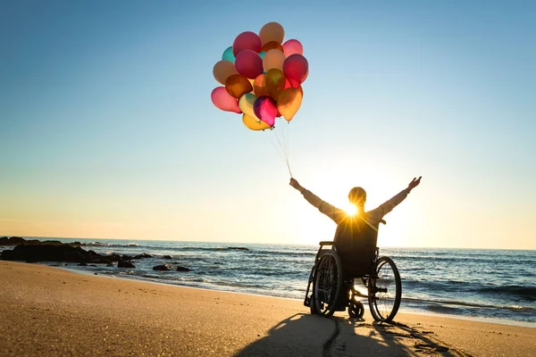 Handikappad Man Rullstolen Med Stigande Händer Och Färgade Ballonger Stranden — Stockfoto