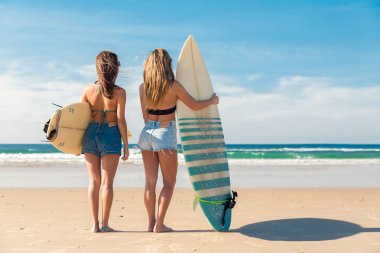 Arkadan görünüş takının kadın arkadaş sörf tahtaları okyanus bakarken holding