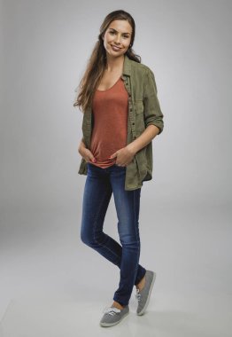 Gülümseyen ve gri arka planda duran güzel genç bir kadın.