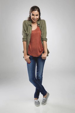 Gri arka planda duran ve gülümseyen güzel genç bir kadın.