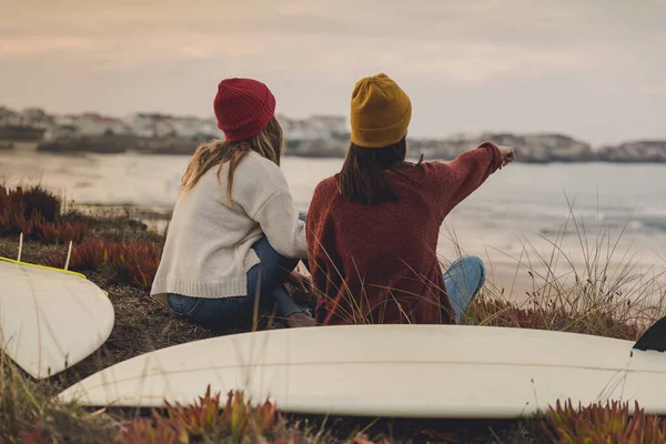 两个最好的朋友与她的冲浪板一起坐在海岸线边 望着大海 — 图库照片