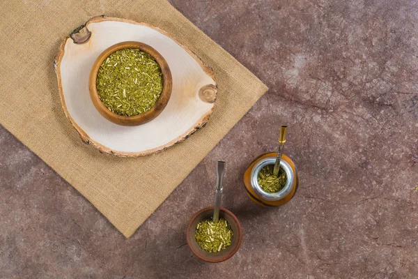 Yerba mate in calabash, in porongo and in wooden bowl on stone background