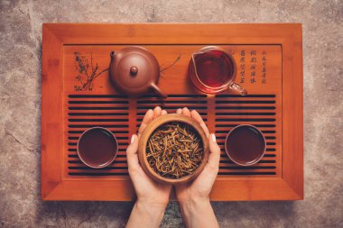 Çin çay seremonisi. Elinde kırmızı çayla ahşap bir çay kasesi tutan kadın. Çaydanlık, kil çay fincanı, çaça ve ahşap kase sehpası çay masasında..