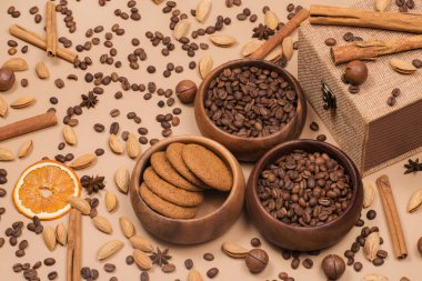 Baharatlı bir kutu kahve ve kurabiye. Bej arkaplanda tarçın, badem ve macadamia..