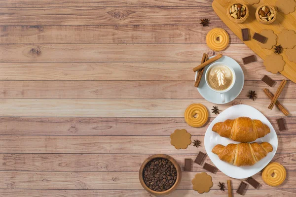 Flat lay cup of coffee, croissants, cookies and chocolate on rustic wooden table. Breakfast at morning. Top view, place for text. Design banner concept
