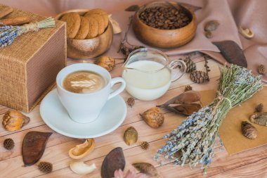 Bir fincan kahve, süt, kahve çekirdeği, ahşap arka planda yulaf ezmeli kurabiye. Sıcak sonbahar kompozisyonu. Sabah kahvaltısı. Sonbahar havası