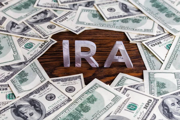 Tahta arka planda gümüş metal harflerden oluşan IRA sözcüğü dolar banknotlarıyla çevrili. — Stok fotoğraf