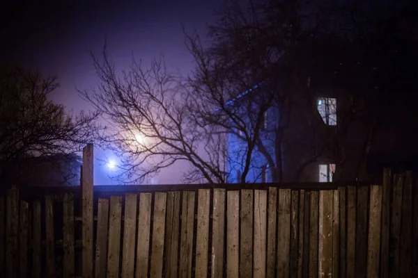 Donker mistig nachtzicht op houten hek en griezelig huis met sele — Stockfoto