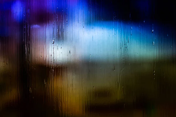 Uno sfondo astratto lampioni notturni bokeh attraverso vetro bagnato con gocce d'acqua, primo piano con messa a fuoco selettiva — Foto Stock
