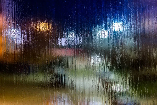 Un fondo abstracto luces de la calle noche bokeh a través de vidrio húmedo, primer plano con enfoque selectivo —  Fotos de Stock