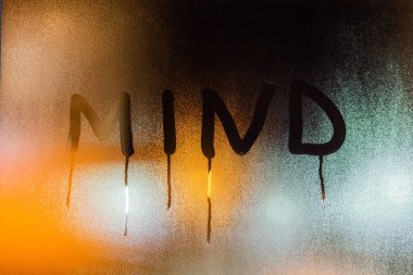 Gece ıslak cam üzerine yazılmış zihin kelimesi. Yakın plan, bulanık turuncu arka plan.