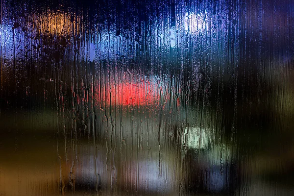 Abstrakcyjne tło nocne światła uliczne bokeh przez mokre szkło, zbliżenie z selektywną ostrością — Zdjęcie stockowe
