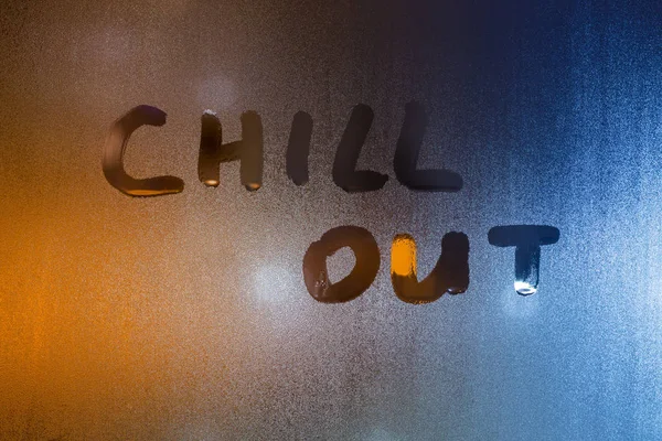 the words chill out written by finger on wet glass with blurred lights in background