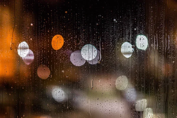 Un fond abstrait lumières de rue nocturnes bokeh à travers verre mouillé avec taches d'eau, gros plan avec mise au point sélective — Photo