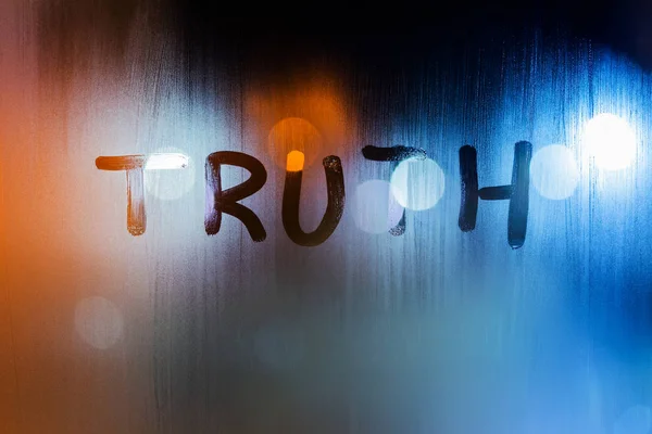 在夜湿的窗玻璃上写的"真理"这个词是背景不正的特写 — 图库照片