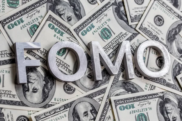 La parola FOMO figurava con lettere in alluminio sullo sfondo delle banconote in dollari USA - con attenzione selettiva Immagine Stock