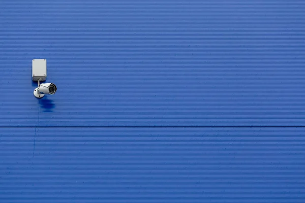 Malá bílá bezpečnostní kamera na velké modré ocelové silo zeď — Stock fotografie