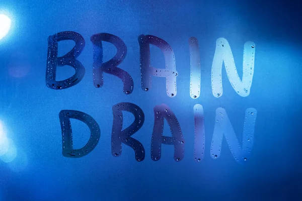 Orden brain drain skrivet på natten vått fönster glas närbild med suddig bakgrund i klassisk blå färg — Stockfoto