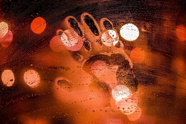 夜湿玻璃上的手印，红色，背面有模糊的街灯 — 图库照片