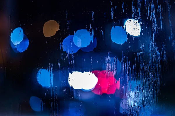 Um fundo abstrato de luzes da polícia vermelho e azul bokeh através de vidro molhado à noite close-up com foco seletivo — Fotografia de Stock