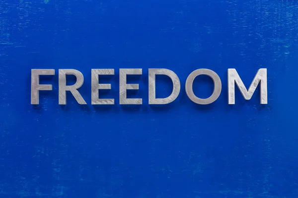 The word freedom laid with silver metal characters on blue painted wooden board in central flat lay composition — 스톡 사진