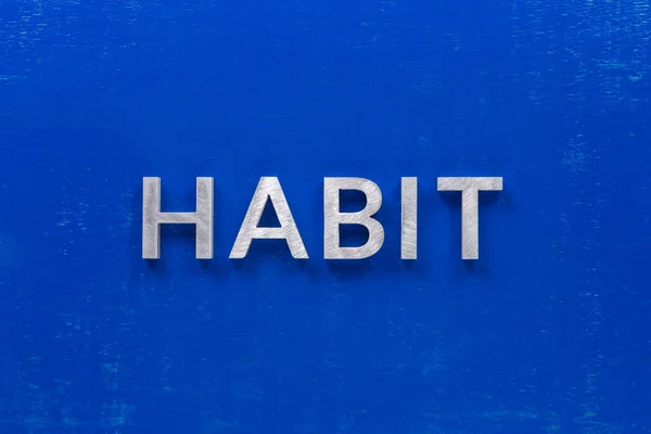 La palabra hábito establecido con caracteres de metal plateado sobre tablero de madera pintado azul en la composición de la disposición plana central —  Fotos de Stock