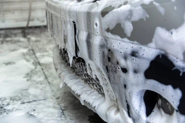 Um nariz de carro coberto por espuma de sabão enquanto se lava em casa - close-up frente wiew com foco seletivo — Fotografia de Stock